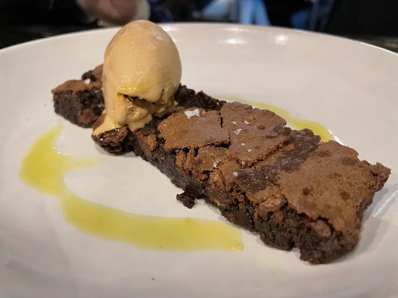 A slice of chocolate brownie with a scoop of ice cream drizzled with sauce