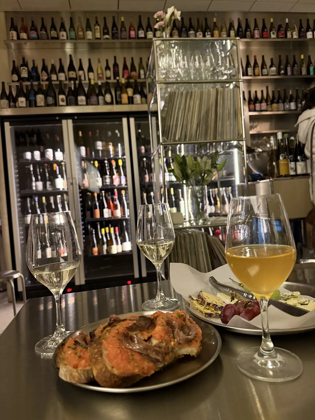A glass of white wine and a beer next to a plate of toast with tomato