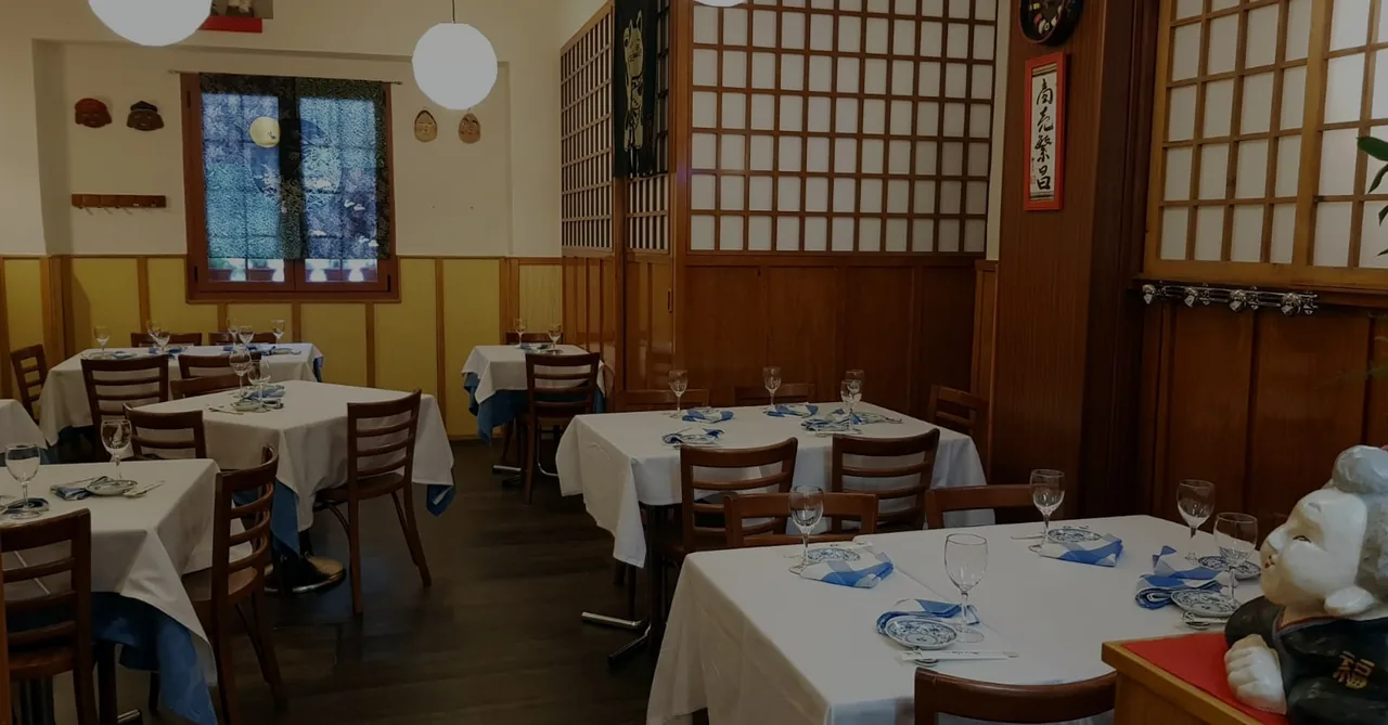 Dining room of white-clothed tables set with blue napkins and wine glasses, wood panelling, shoji screens, hanging paper globe lights and framed Japanese calligraphy on the walls