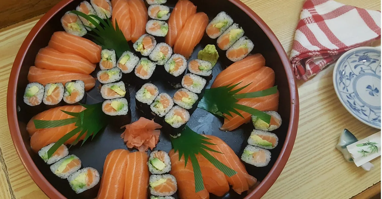 A round black tray of salmon nigiri and salmon and avocado maki rolls arranged in a circle