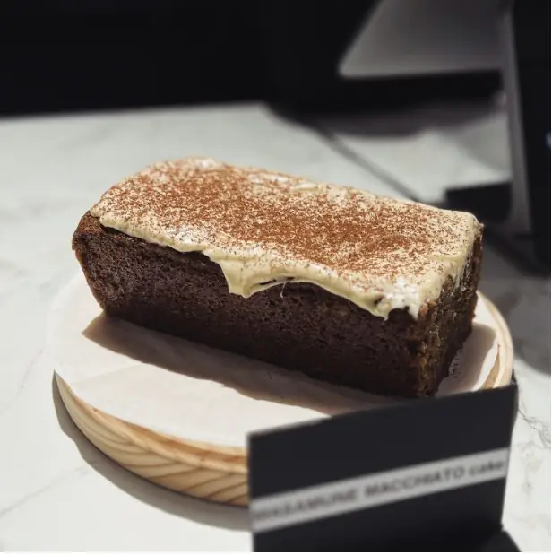 Frosted loaf cake dusted with cinnamon on a round wooden board, small printed label card leaning in front