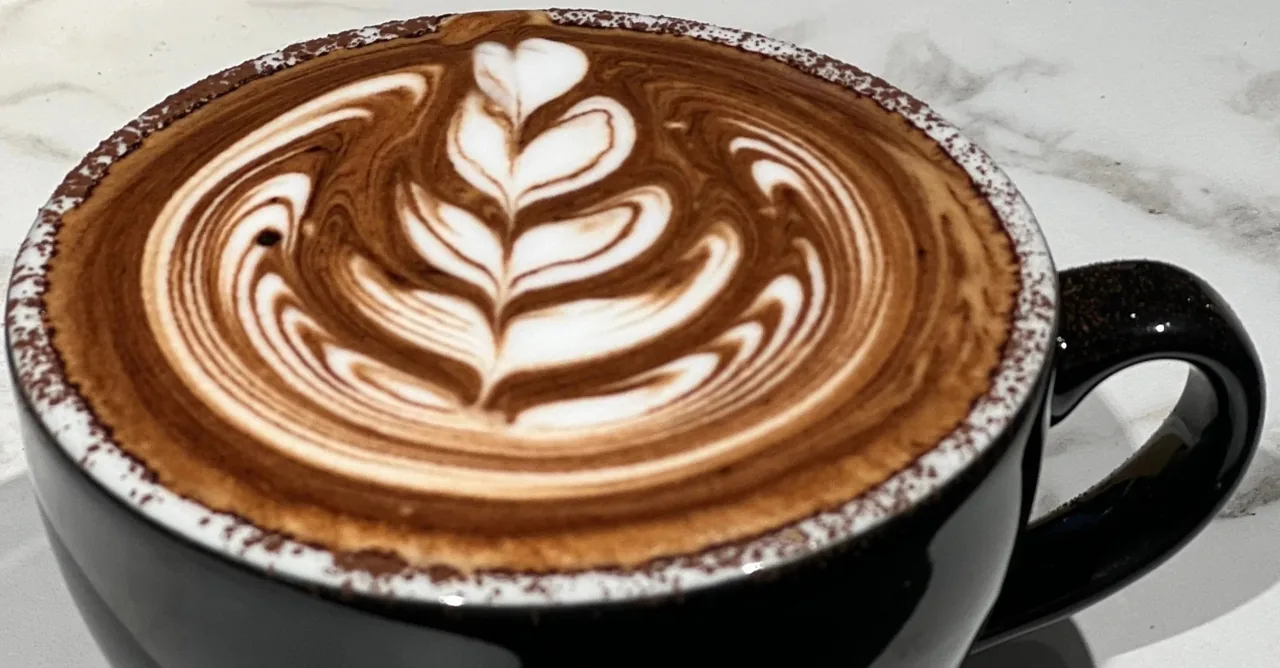 A close view of a latte with a detailed leaf pattern in a black cup