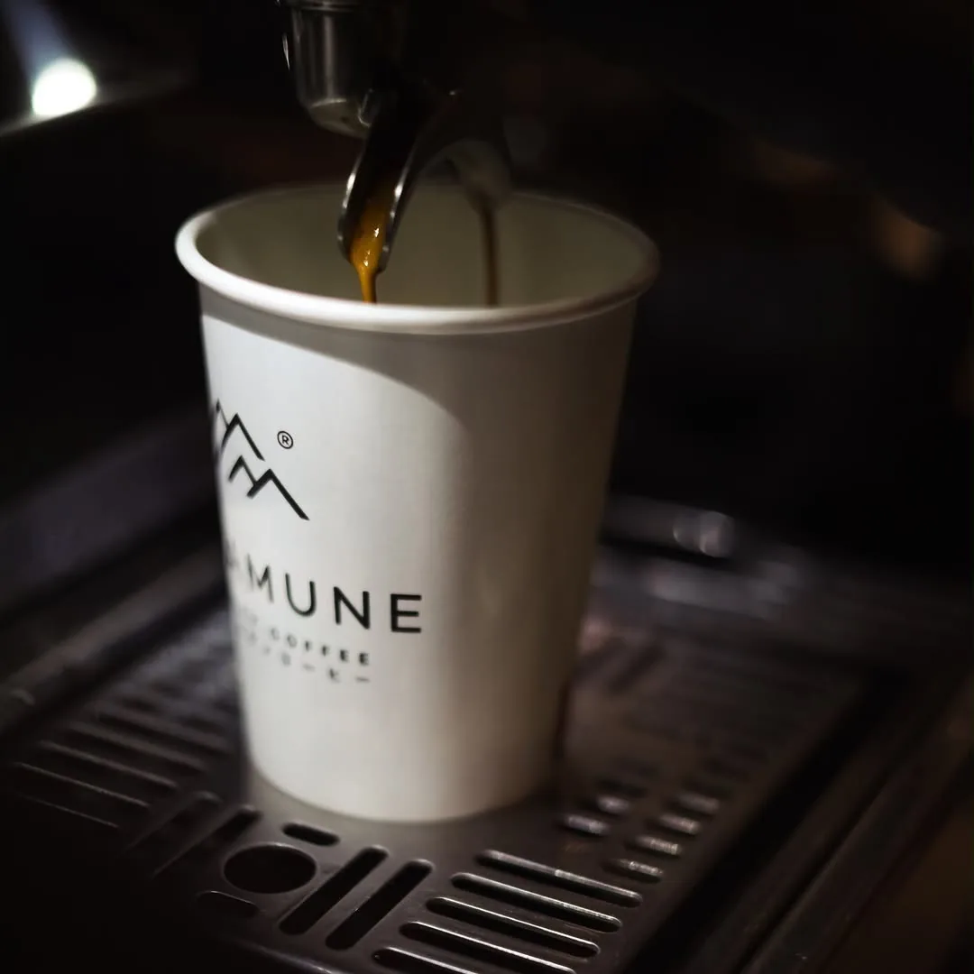 Coffee pouring from an espresso machine into a white takeaway cup