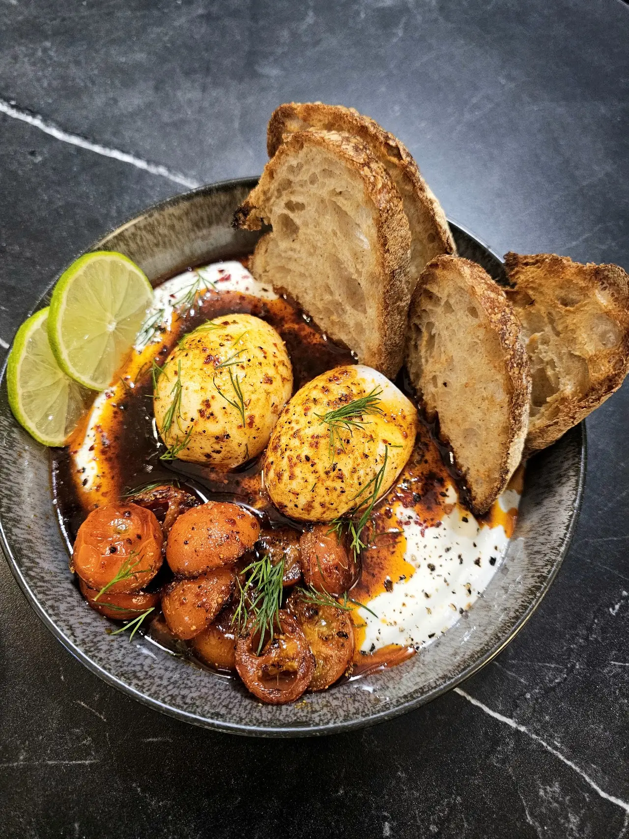 A brunch bowl of soft-boiled eggs and roasted carrots with toasted bread and a lime wedge