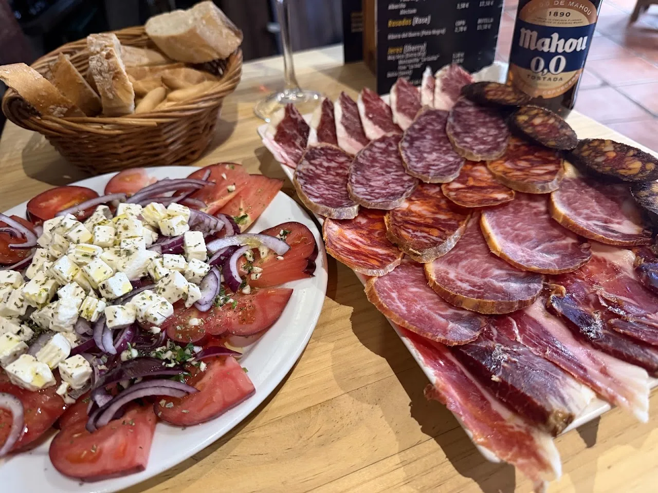 A platter of sliced cured ham and sausage with a tomato and red onion salad, served with bread