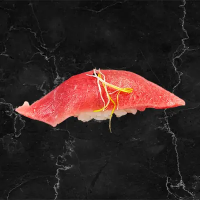 Fatty tuna (toro) nigiri sushi topped with fine garnish threads on a dark marble surface