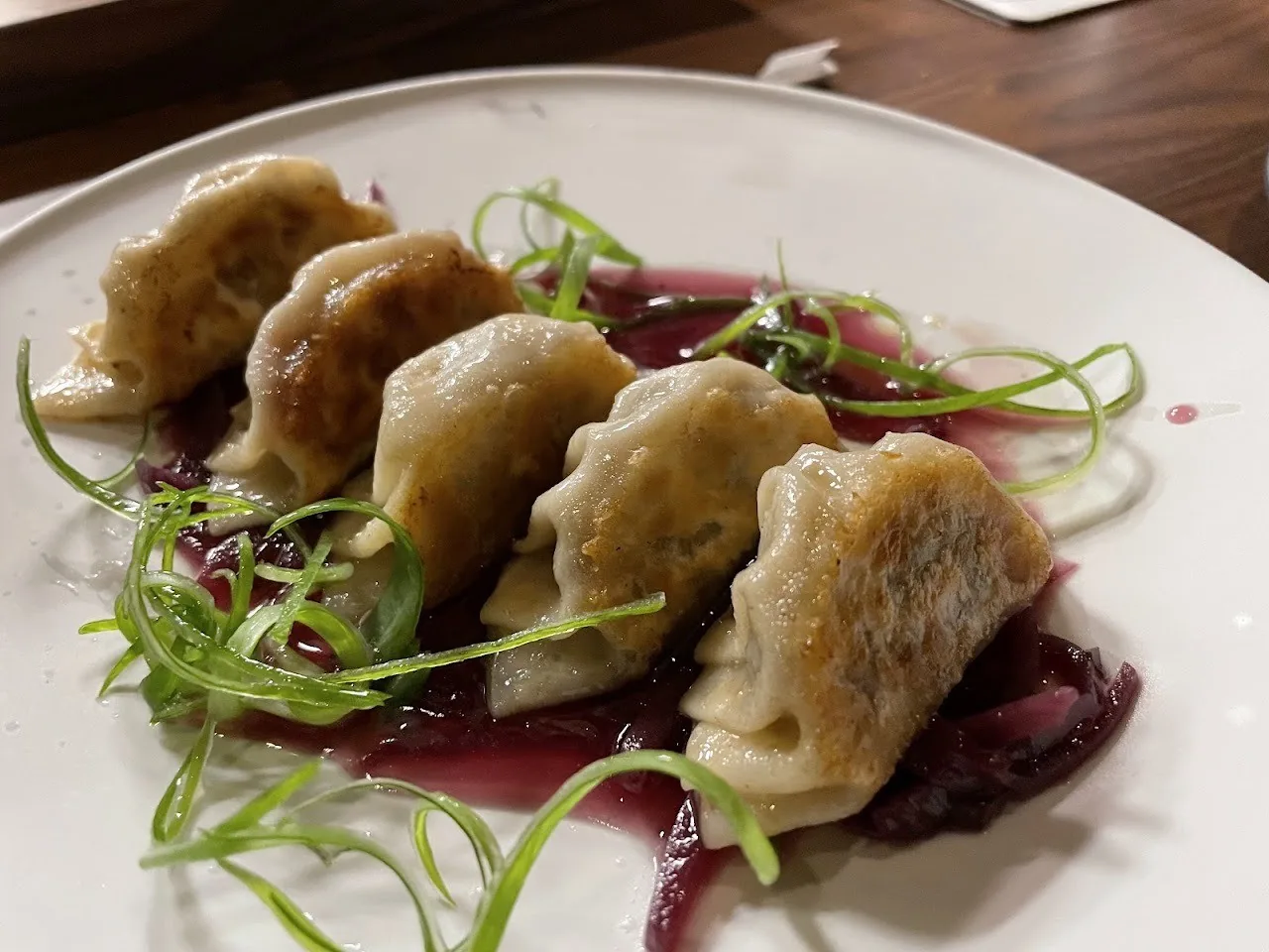 Pan-fried gyoza on a white plate with purple sauce and green onion