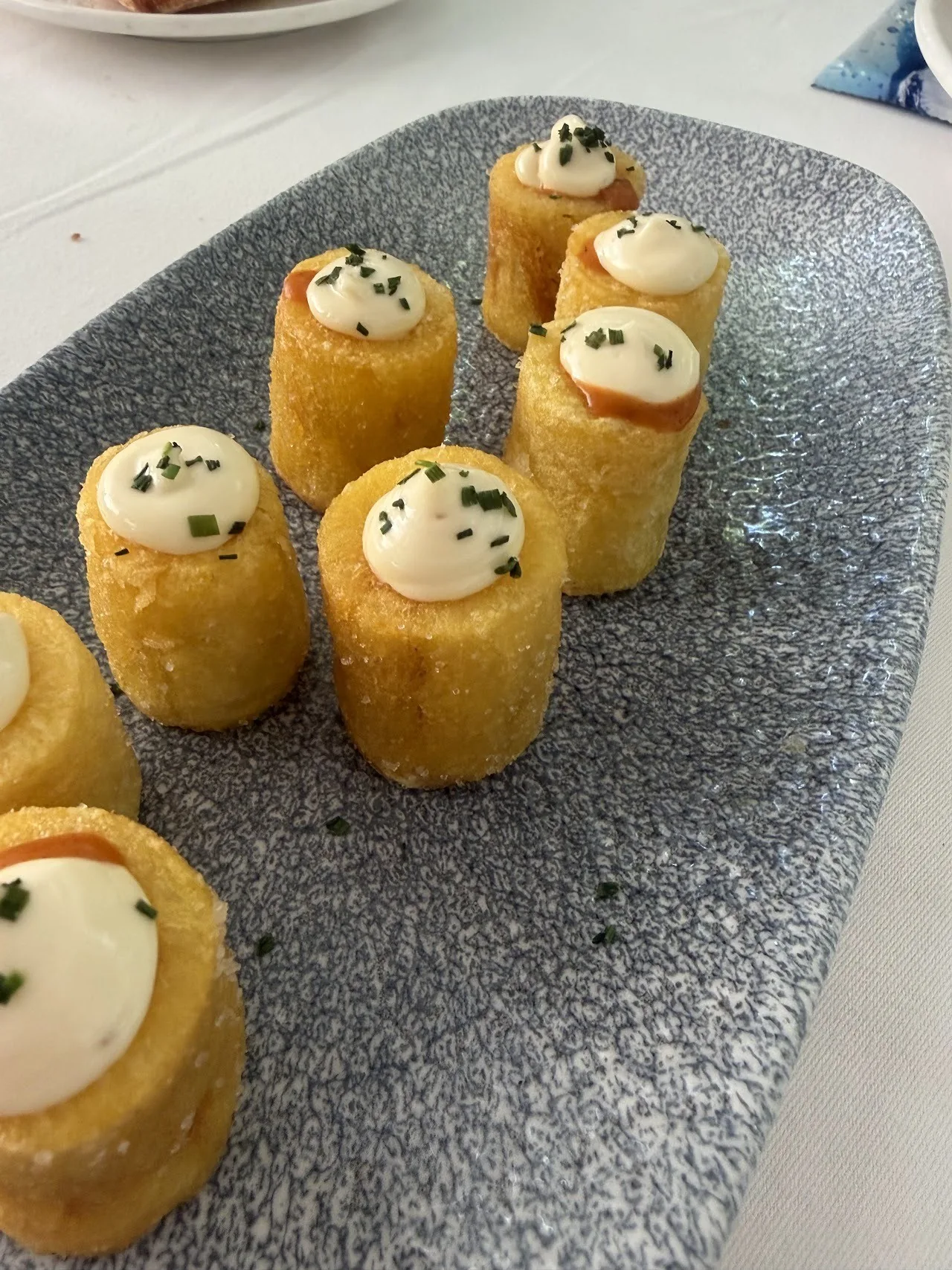 Fried croquette cylinders topped with cream on a grey platter