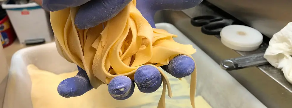 Gloved hands holding freshly cut tagliatelle pasta over a floured tray