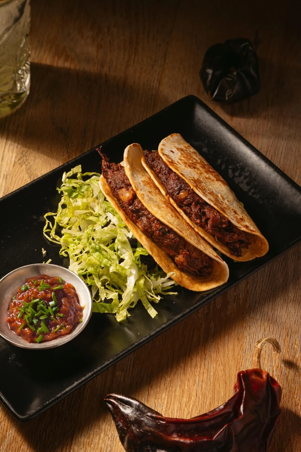 Three folded tacos on a black tray with shredded cabbage and a small bowl of salsa