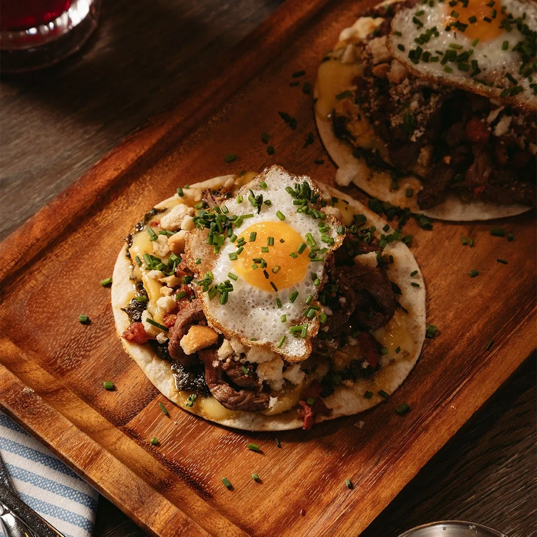 A tostada topped with shredded meat, herbs and a fried egg on a wooden board