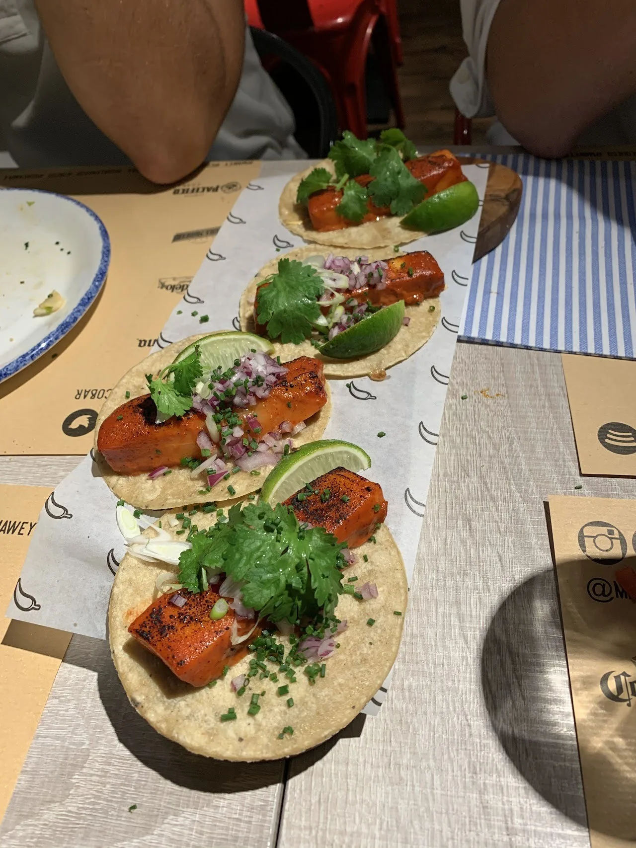 Several tacos topped with red onion and herbs lined up on a paper-covered table