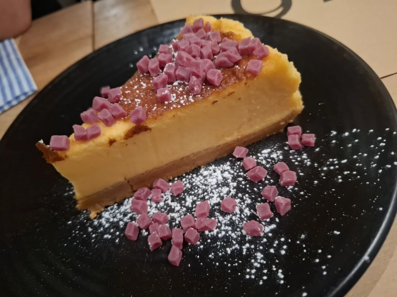 A slice of flan-style dessert with a diced pink garnish and powdered sugar