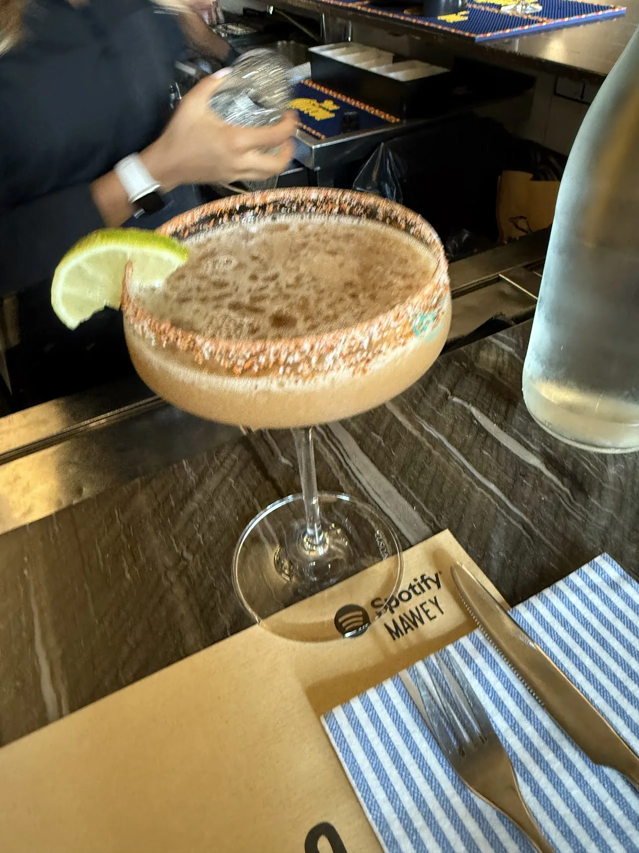 A frothy cocktail in a coupe glass garnished with a lime wedge
