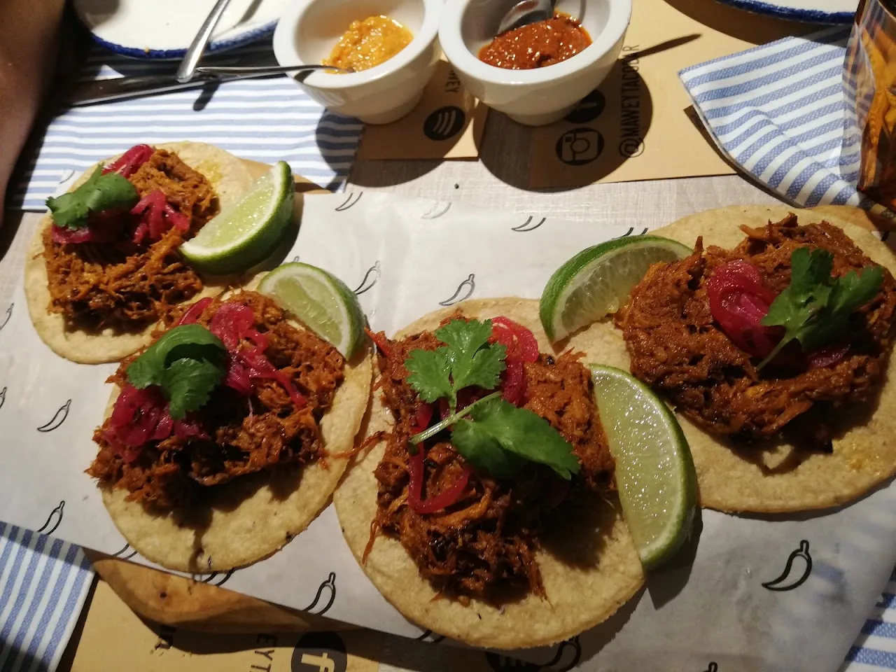 A platter of soft tacos with shredded meat, lime wedges and fresh greens