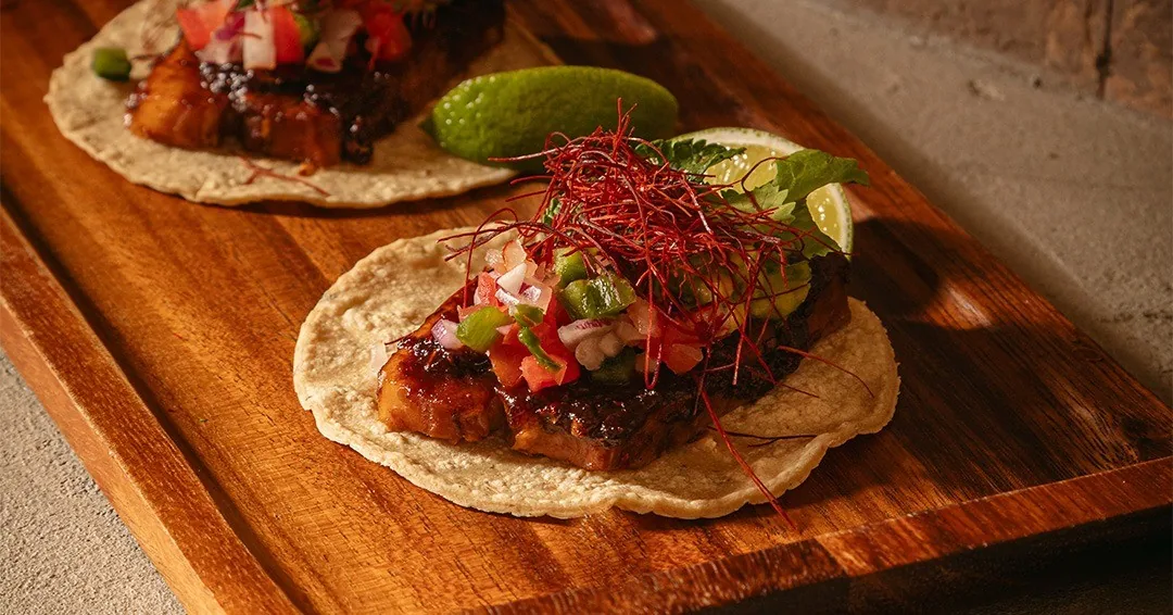 Two tacos with fresh salsa and lime on a wooden board