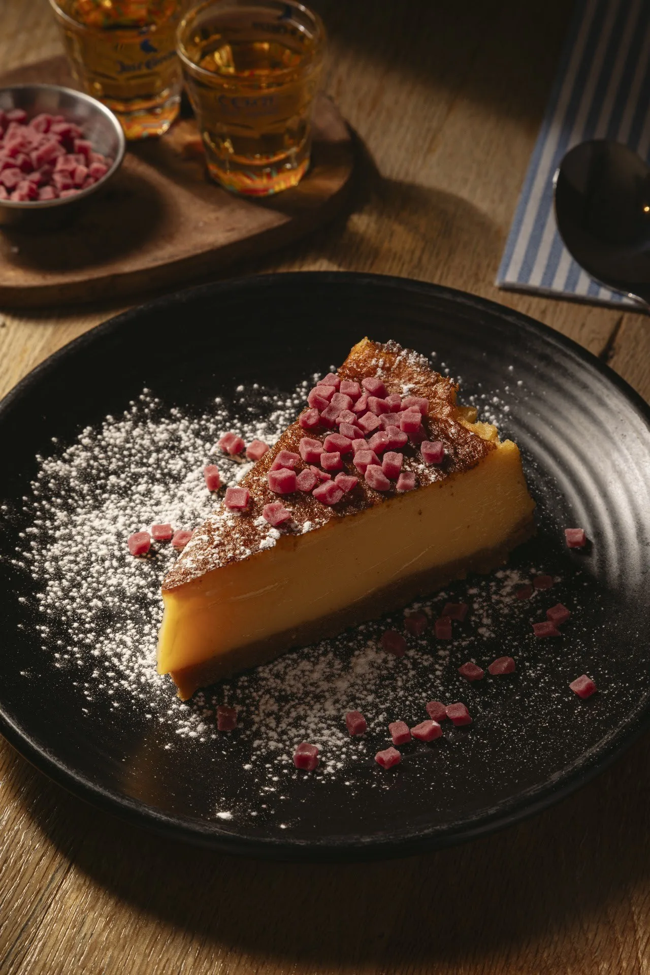 A slice of cake with a dusting of sugar and berries on a black plate