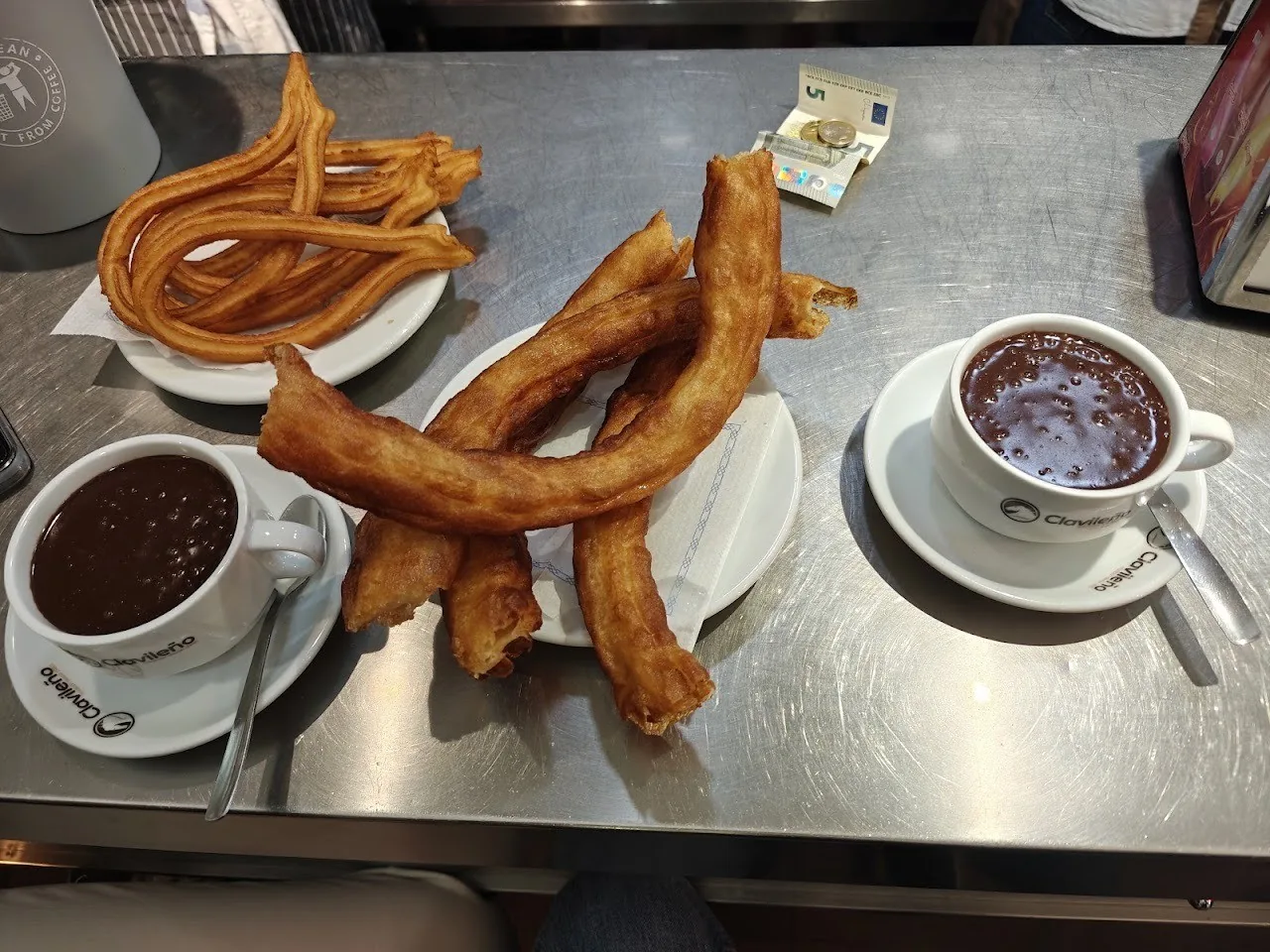 A plate of churros and a cup of hot chocolate on a steel table