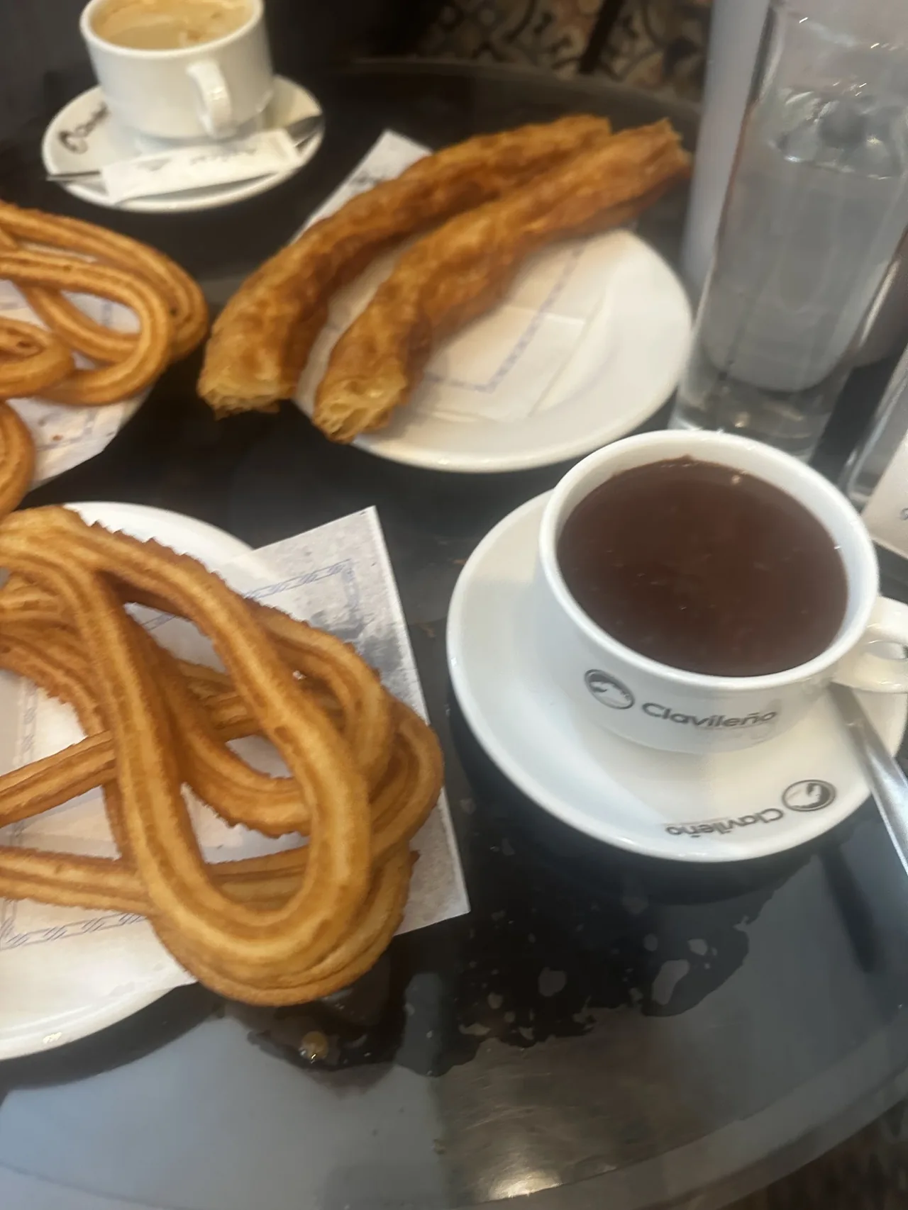 A cup of hot chocolate beside plates of looped churros