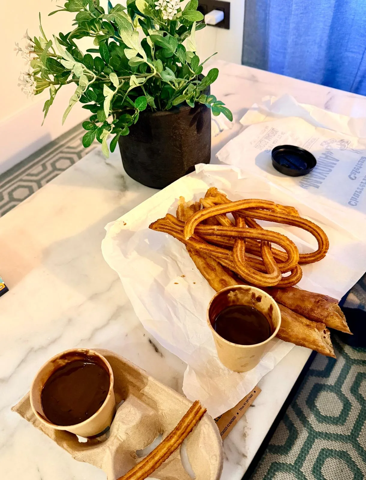 Churros wrapped in paper next to a cup of hot chocolate