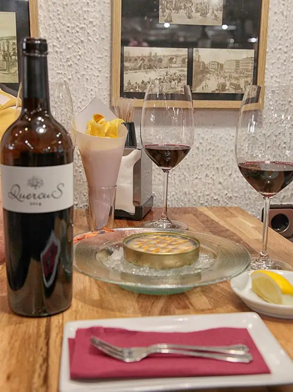Close view of the same table setting with the Quercus wine bottle, two red-wine glasses and a chilled dish on ice