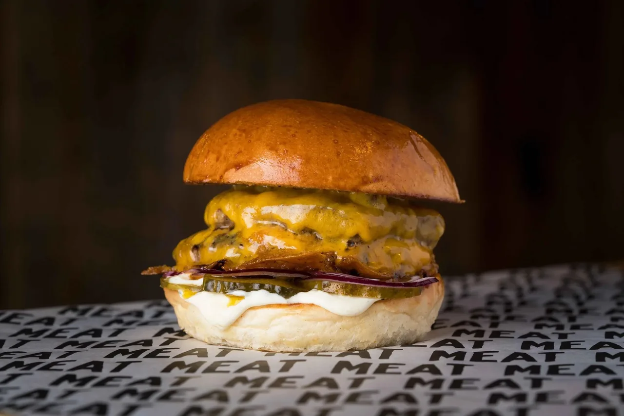 A burger with melted cheese and a glossy bun on printed paper against a dark background