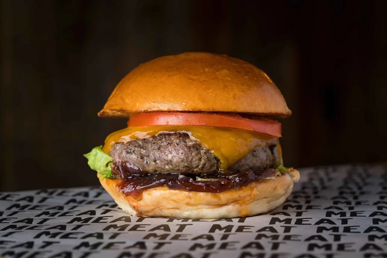 A burger with a tomato slice, cheese and a glossy bun on printed paper