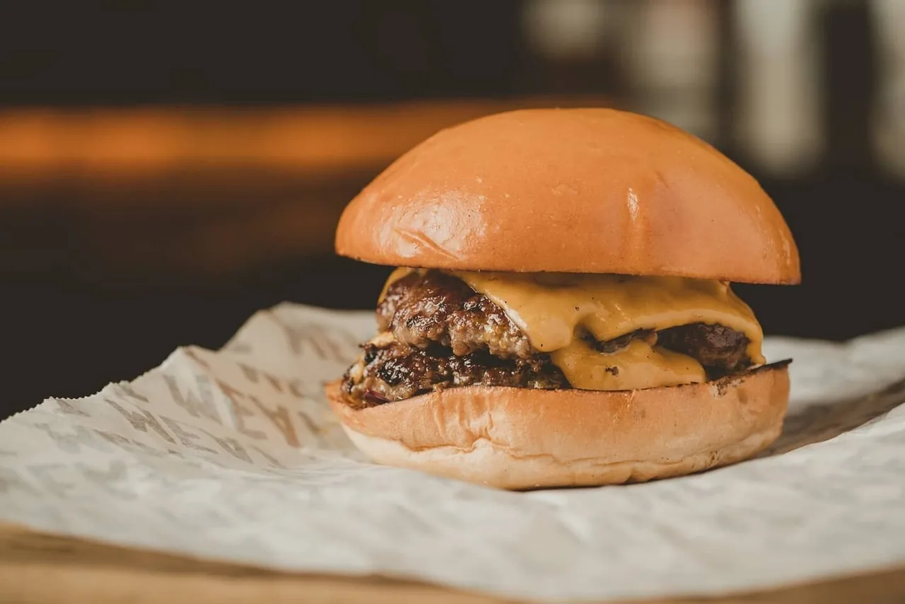 A cheeseburger on white paper on a table in warm light