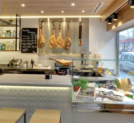 Melgar bar counter with cured Iberian hams hanging on a rack, a chalkboard price list and a chilled seafood display case of shellfish