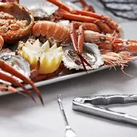 Seafood platter of langoustines, prawns and oysters with a lemon half on a white tray beside seafood scissors