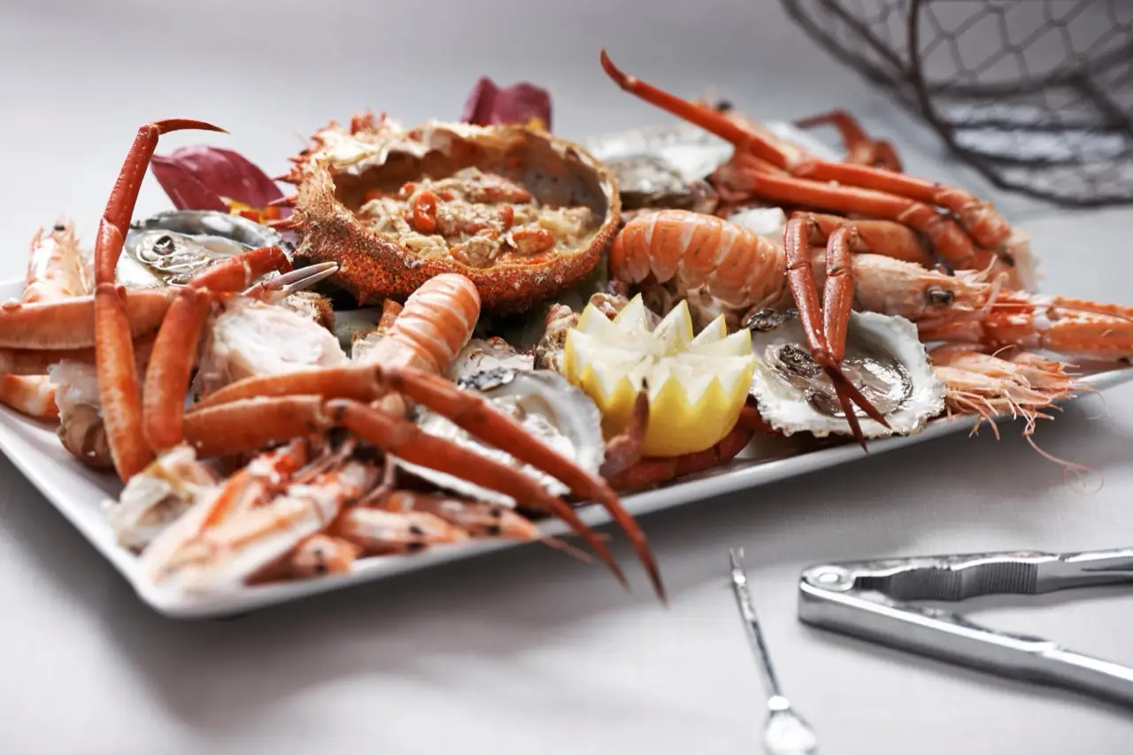 Large seafood platter with a whole spider crab, langoustines, oysters and a carved lemon on a white plate beside seafood crackers