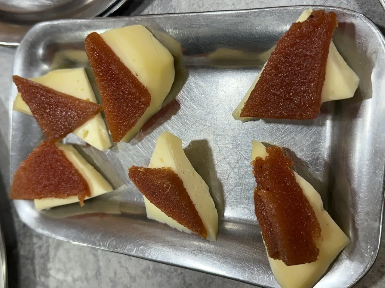 Slices of quince paste on cheese wedges in a metal tray