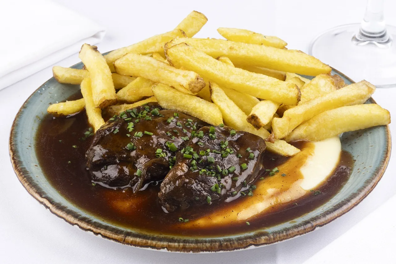 A blue-rimmed plate of braised meat in dark sauce with fries