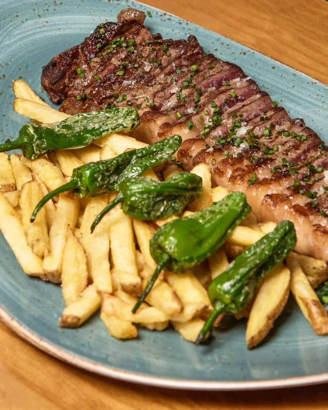A blue plate of sliced grilled steak with fries and green peppers