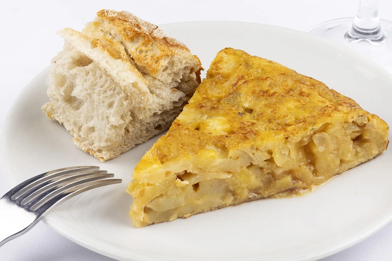 A wedge of potato omelette with a piece of bread on a white plate