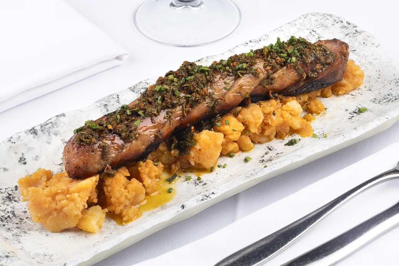 A grilled cut of meat over a base on a long white plate