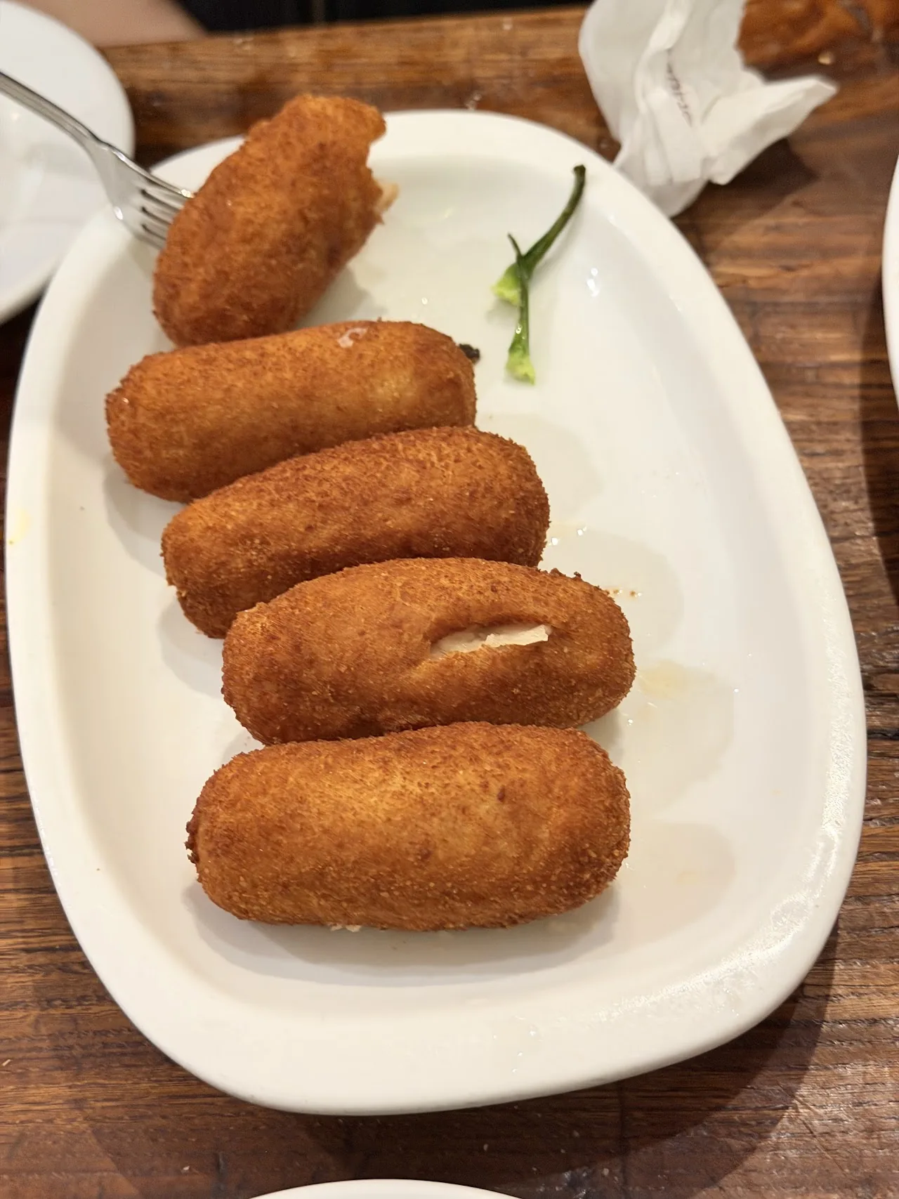 Five golden fried croquetas on an oval plate