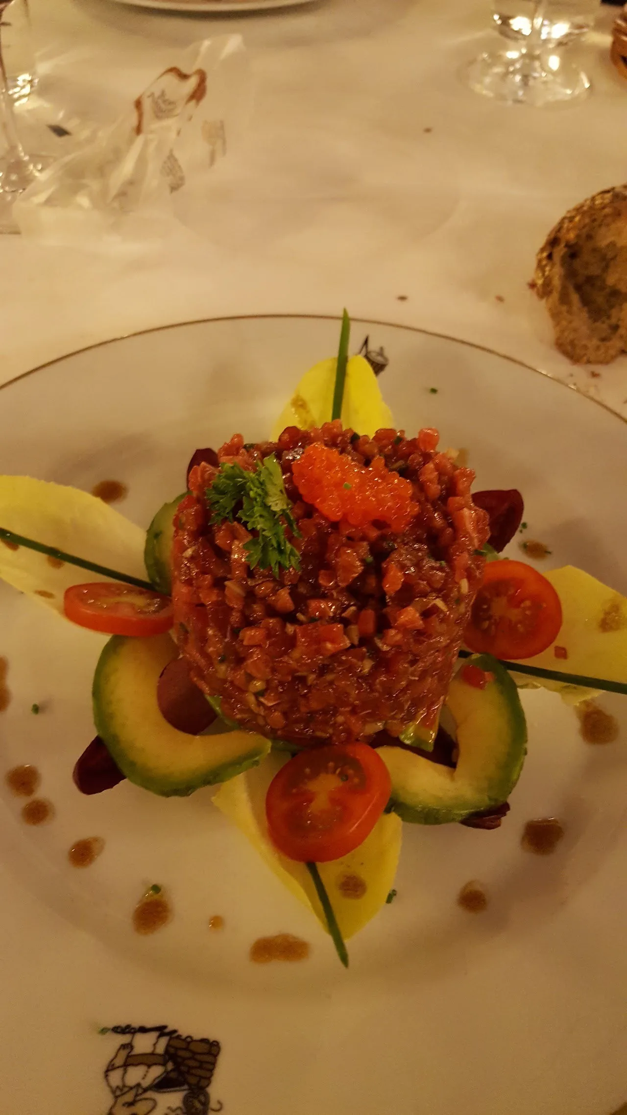 A round mound of red tartare garnished with avocado and tomato on a plate