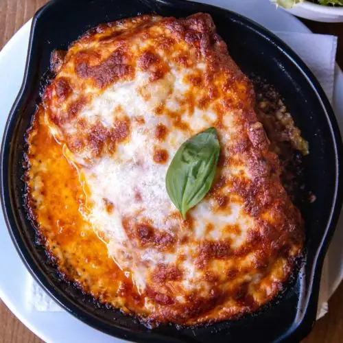 Cheese-topped lasagna baked in a black skillet, garnished with a fresh basil leaf, at Messié Pizza Gluten Free Gràcia.