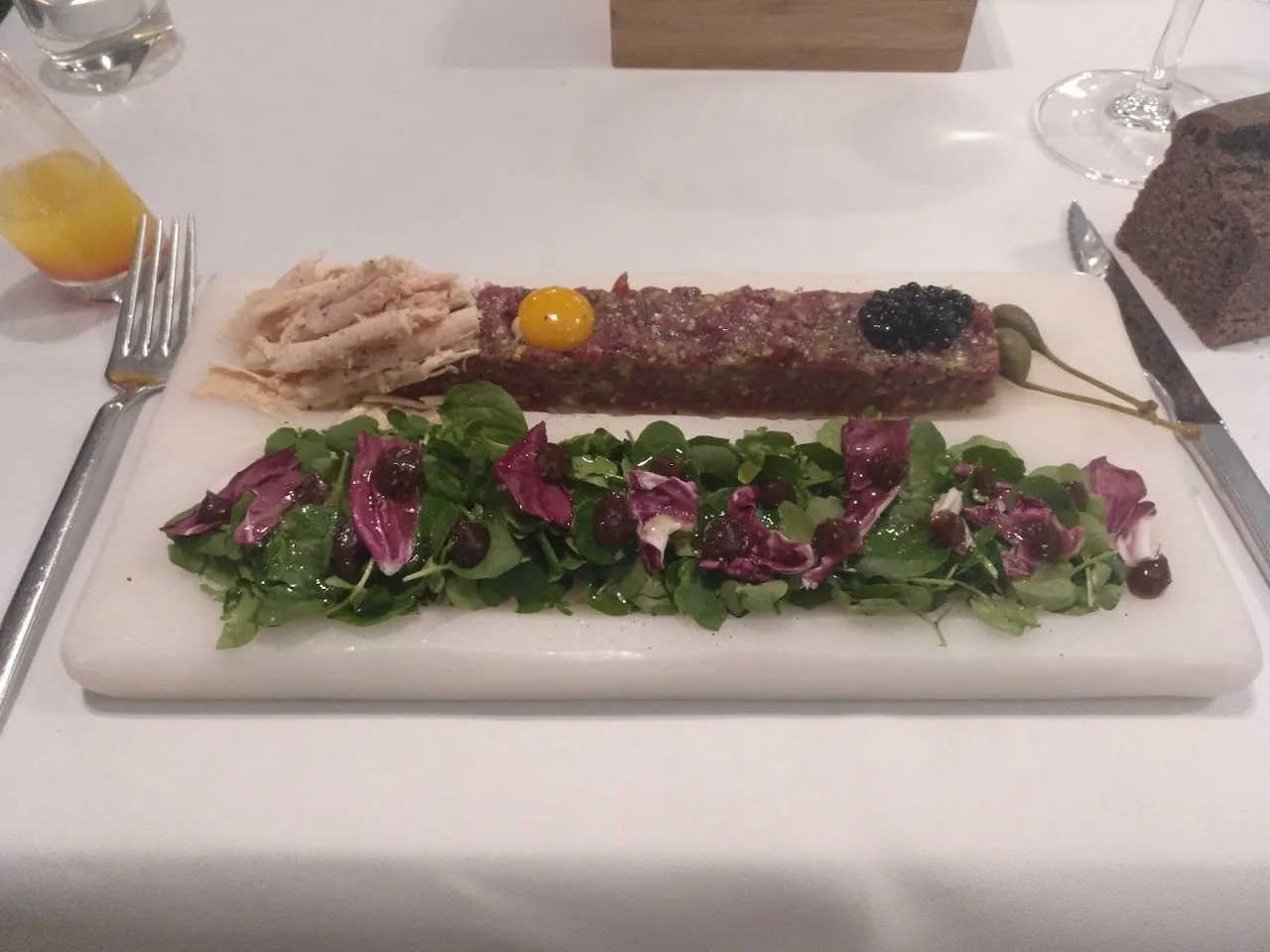 A beef tartare plated on a long dish over mixed greens