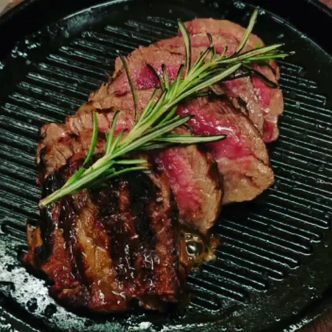 A seared steak in a grill pan garnished with rosemary