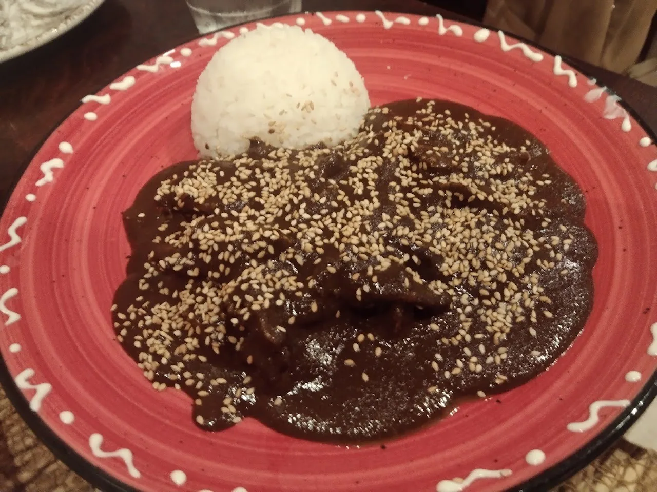A red plate with dark sauce topped with sesame seeds and a scoop of white rice