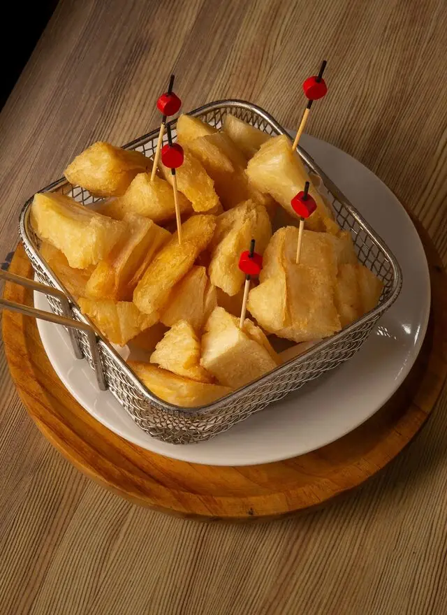 Fried cassava (mandioca frita) wedges skewered with cocktail picks in a metal fry basket on a white plate, Mi Casa Bar y Restaurante