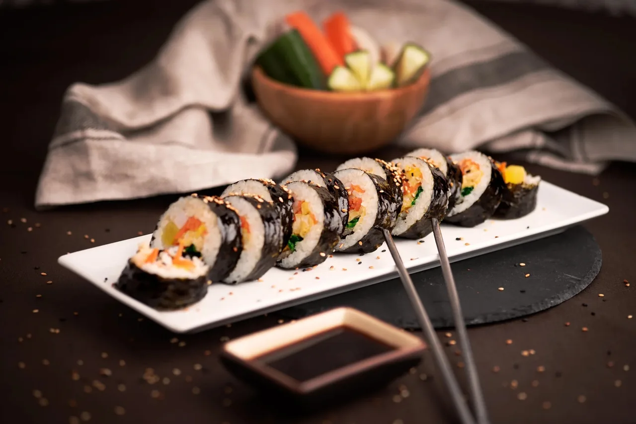 Sliced seaweed rice rolls on a long white plate with a small dish of soy sauce