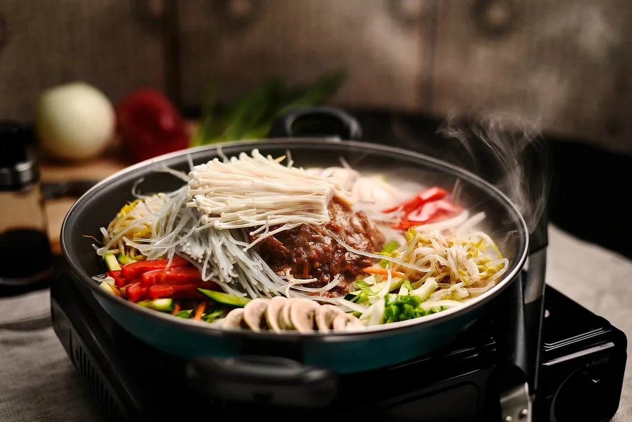 A pot of hot pot with sliced meat, glass noodles, mushrooms and vegetables on a portable stove