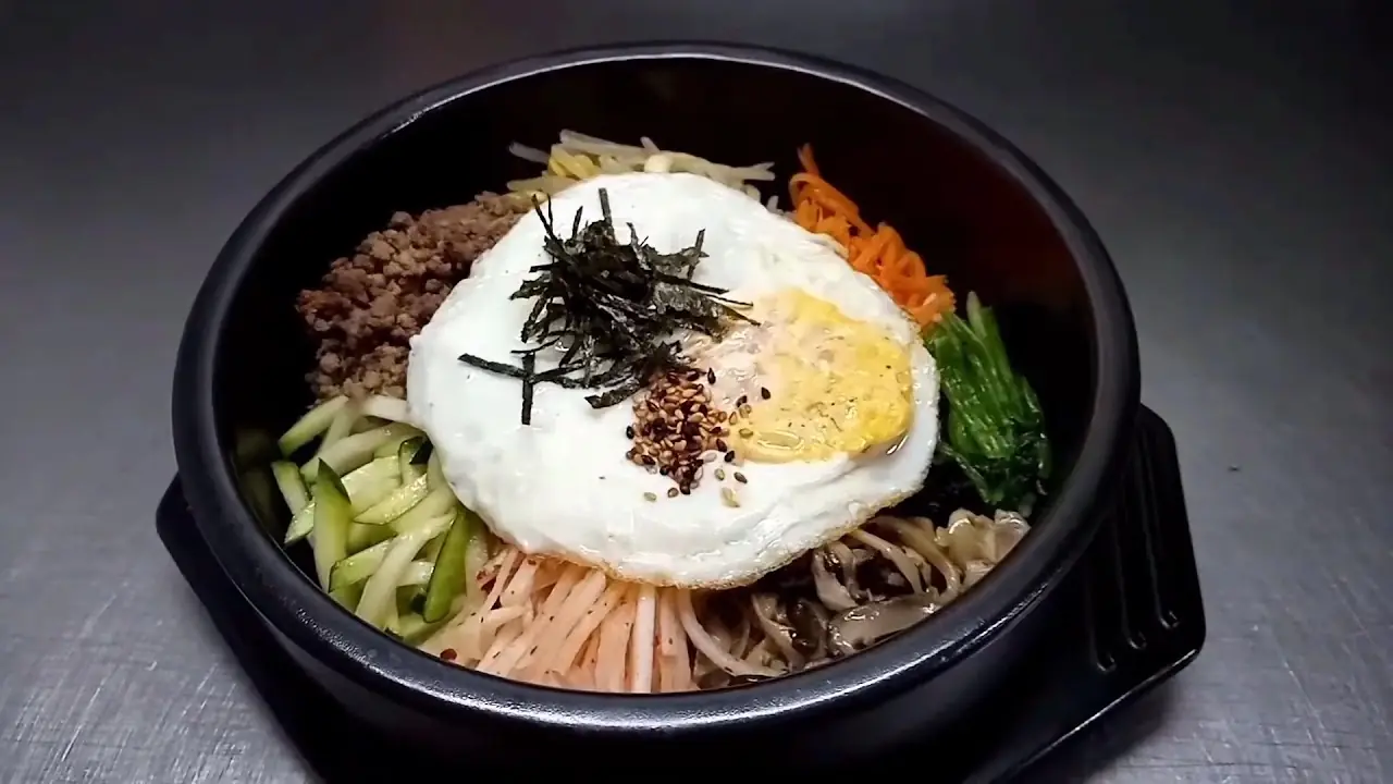 Bibimbap in a black stone bowl topped with a fried egg, seaweed and vegetables