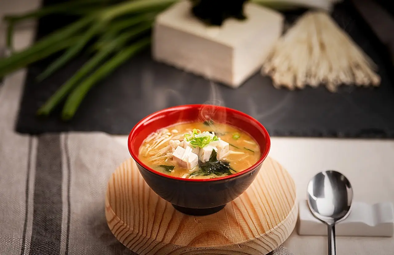 A red bowl of soup with tofu and seaweed on a wooden stand