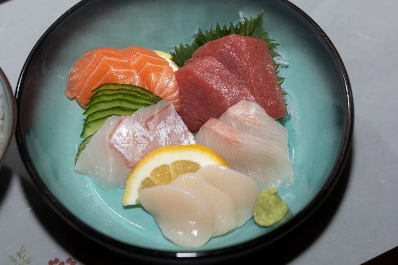A teal bowl of assorted sashimi with lemon and wasabi
