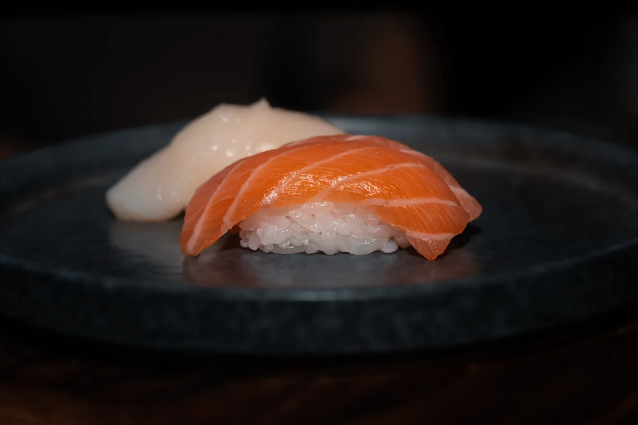 Two pieces of nigiri, one of salmon, on a dark round plate