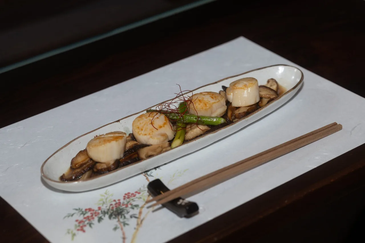 Grilled scallops with asparagus on a long oval plate beside chopsticks